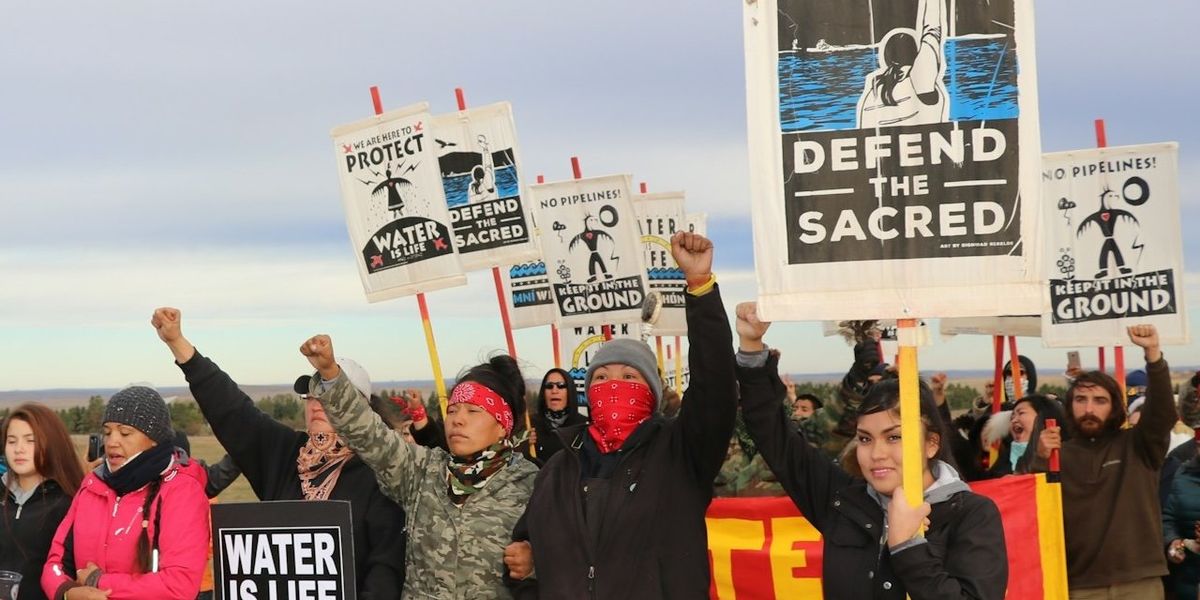 Dakota Access Pipeline protesters hold signs and raise fists.