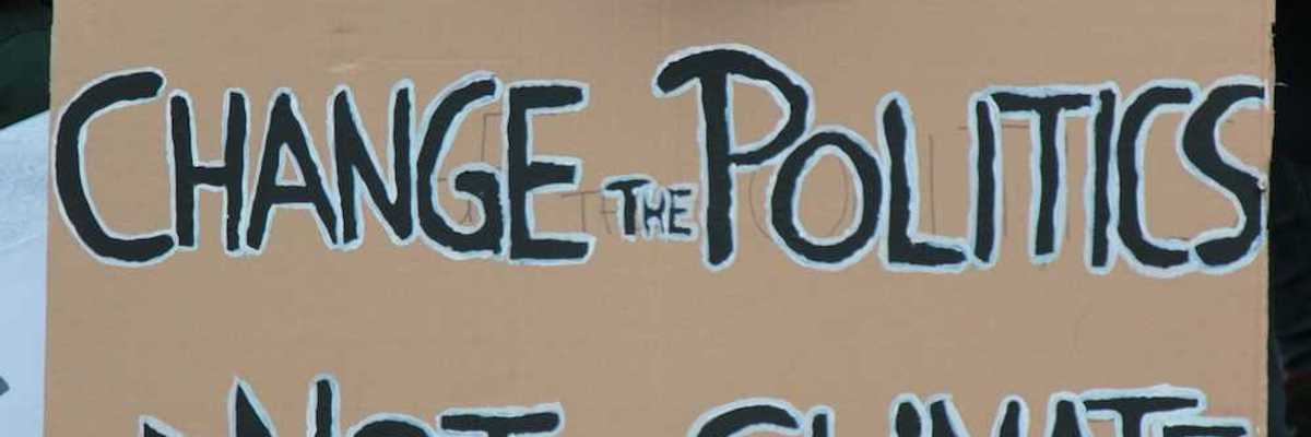 Demonstrator holding a sign reading "CHANGE THE POLITICS, NOT THE CLIMATE"