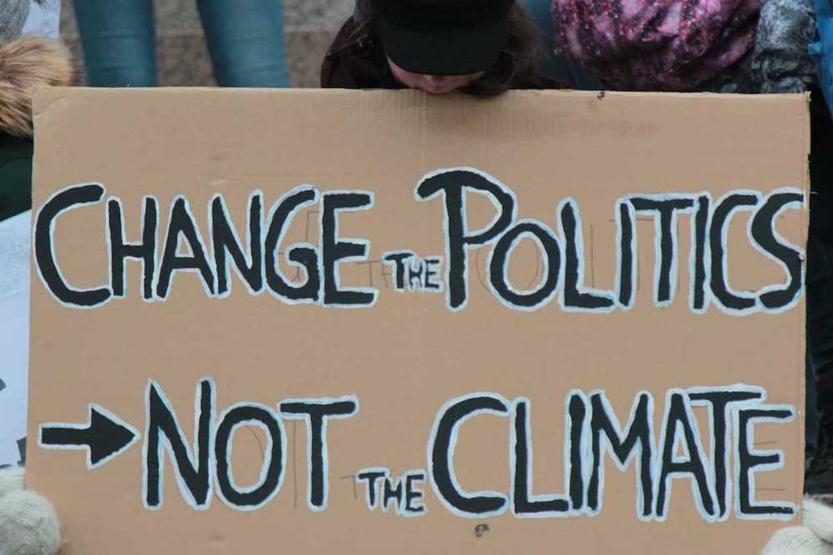 Demonstrator holding a sign reading "CHANGE THE POLITICS, NOT THE CLIMATE"
