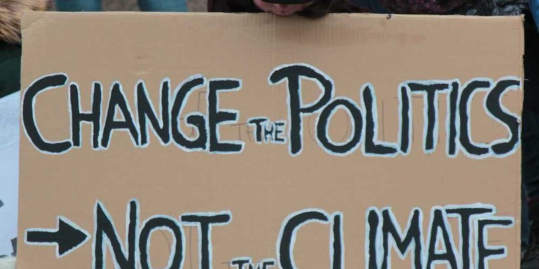 Demonstrator holding a sign reading "CHANGE THE POLITICS, NOT THE CLIMATE"