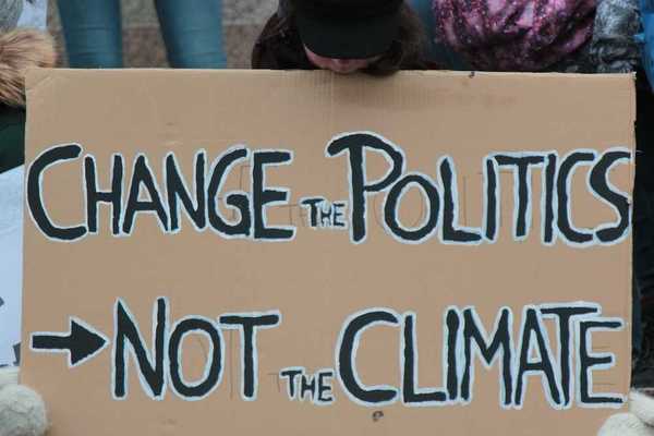 Demonstrator holding a sign reading "CHANGE THE POLITICS, NOT THE CLIMATE"