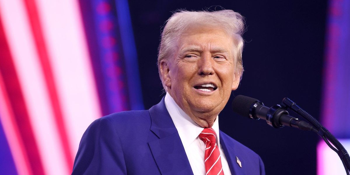 Donald Trump cracks a crooked smile while standing at a microphone.
