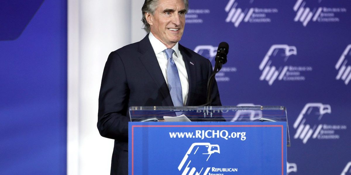 Doug Burgum speaks at a podium wearing a suit and tie.