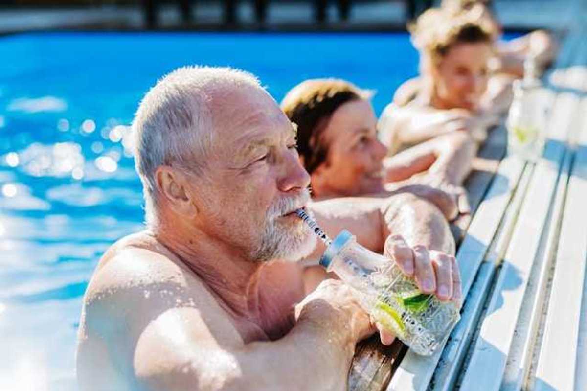Elderly white man in a pool drinking from a straw