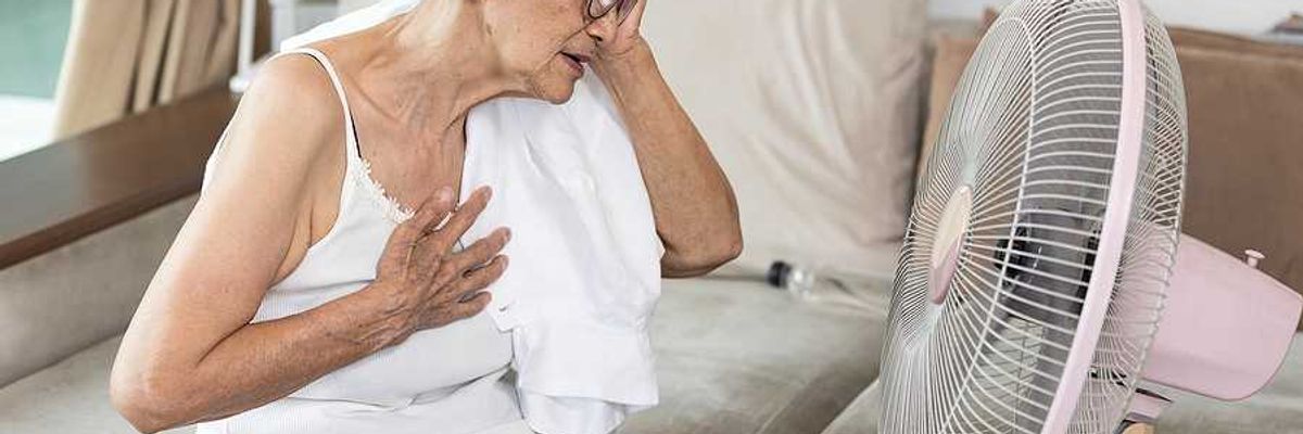 Elderly woman sitting in front of a fan with her hand to her head