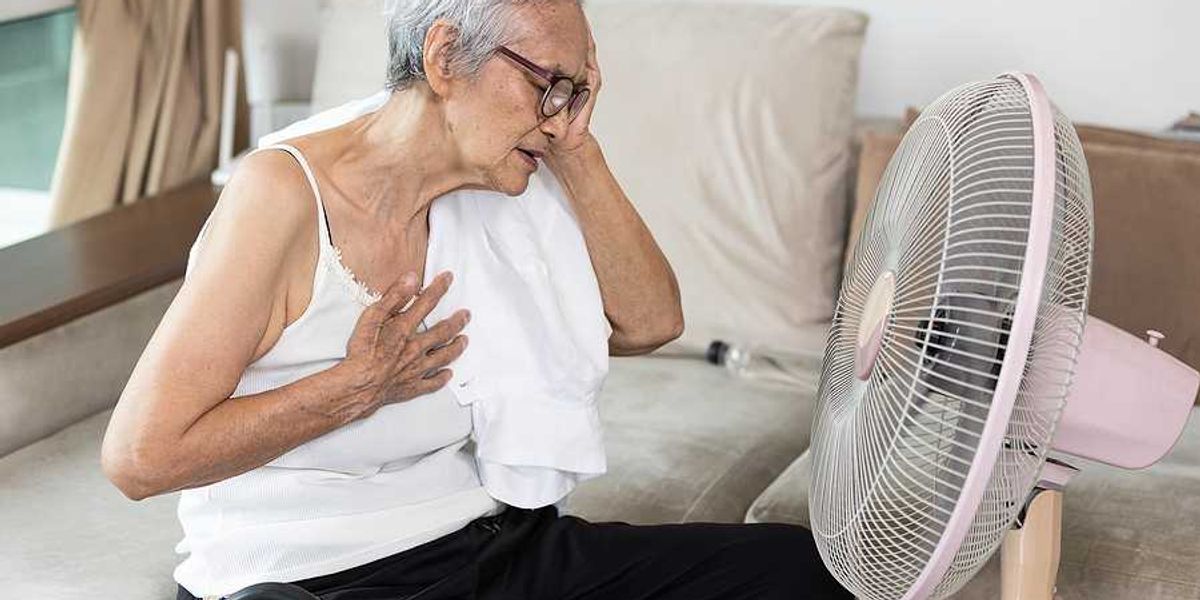 Elderly woman sitting in front of a fan with her hand to her head