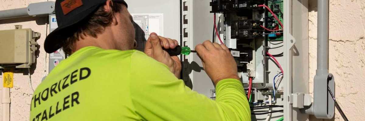 Electrician in yellow-green shirt using a screwdriver while working on an electrical service panel