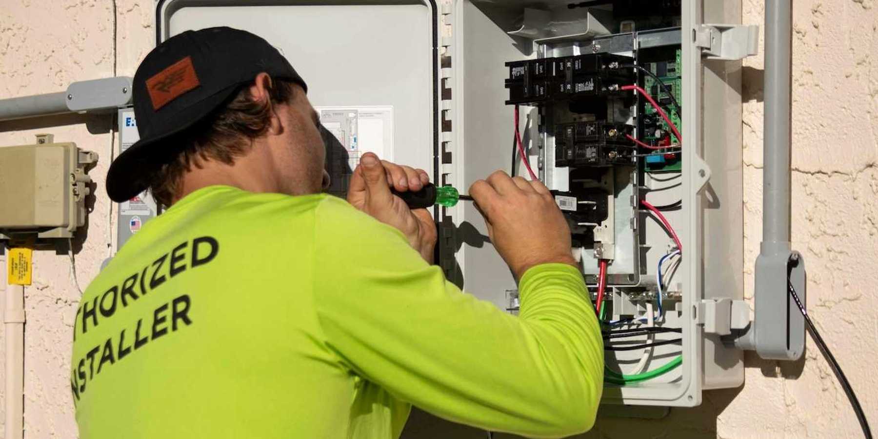 Electrician in yellow-green shirt using a screwdriver while working on an electrical service panel