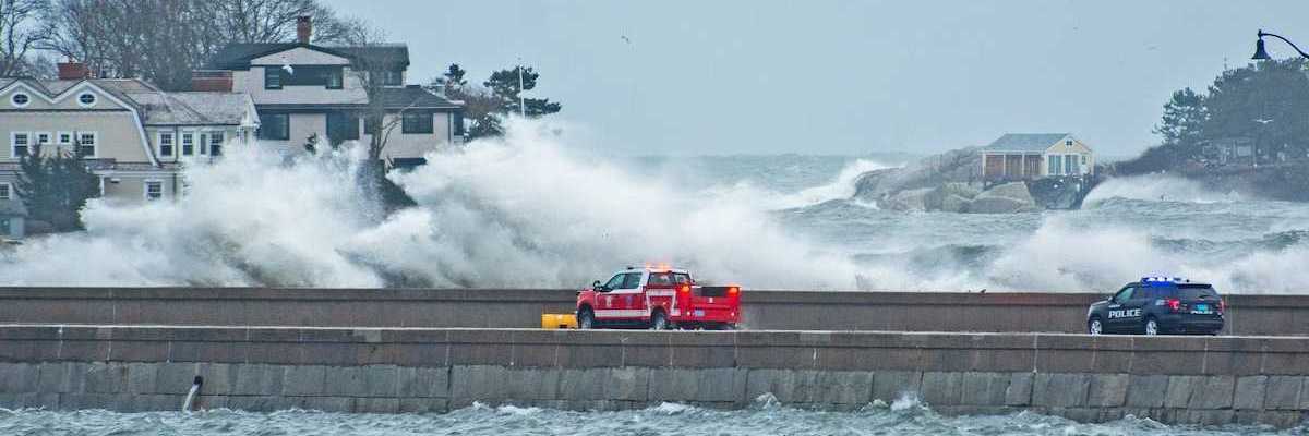 Emergency vehicles — pickup truck and police vehicle traveling amidst with storm-whipped surf