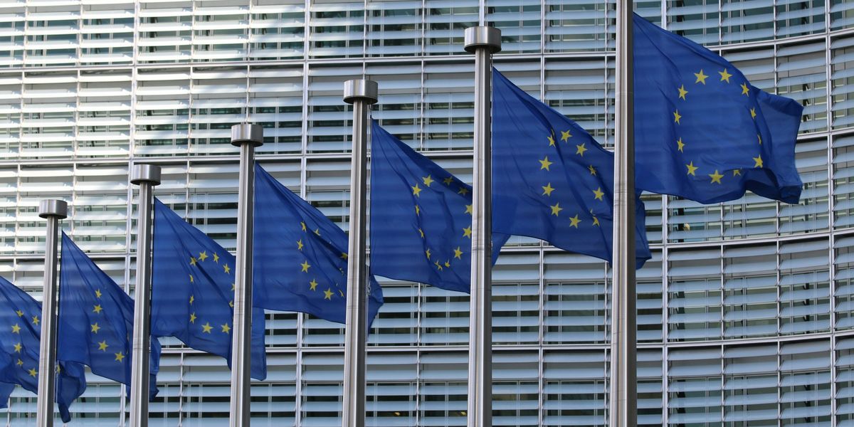 European flags with yellow stars in a circle on a blue background, outside the European Commission building.