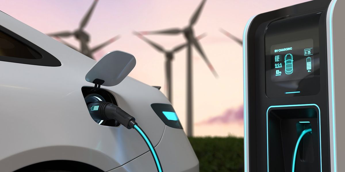 EV charging with wind turbines silhouetted in background against an evening sky.