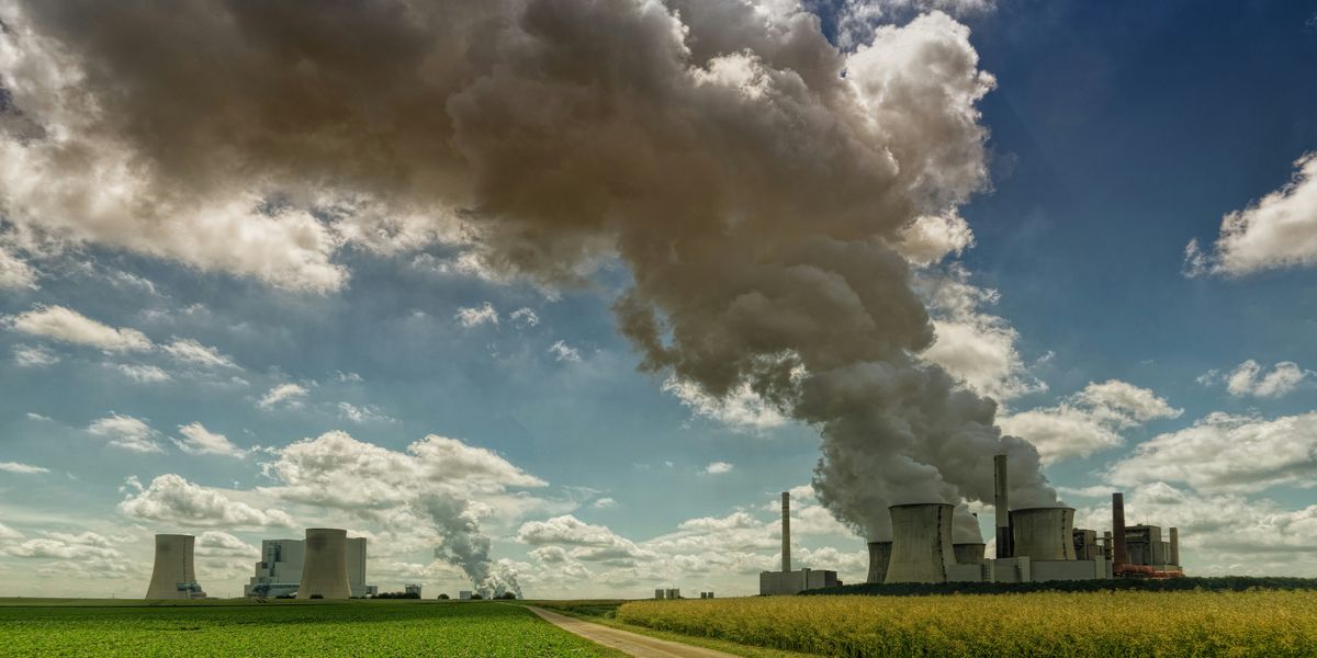factory during daytime with smoke billowing above farm crops.