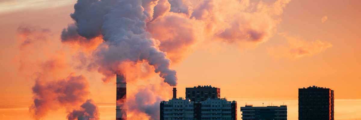 Factory smokestacks emitting smoke against sunset sky.