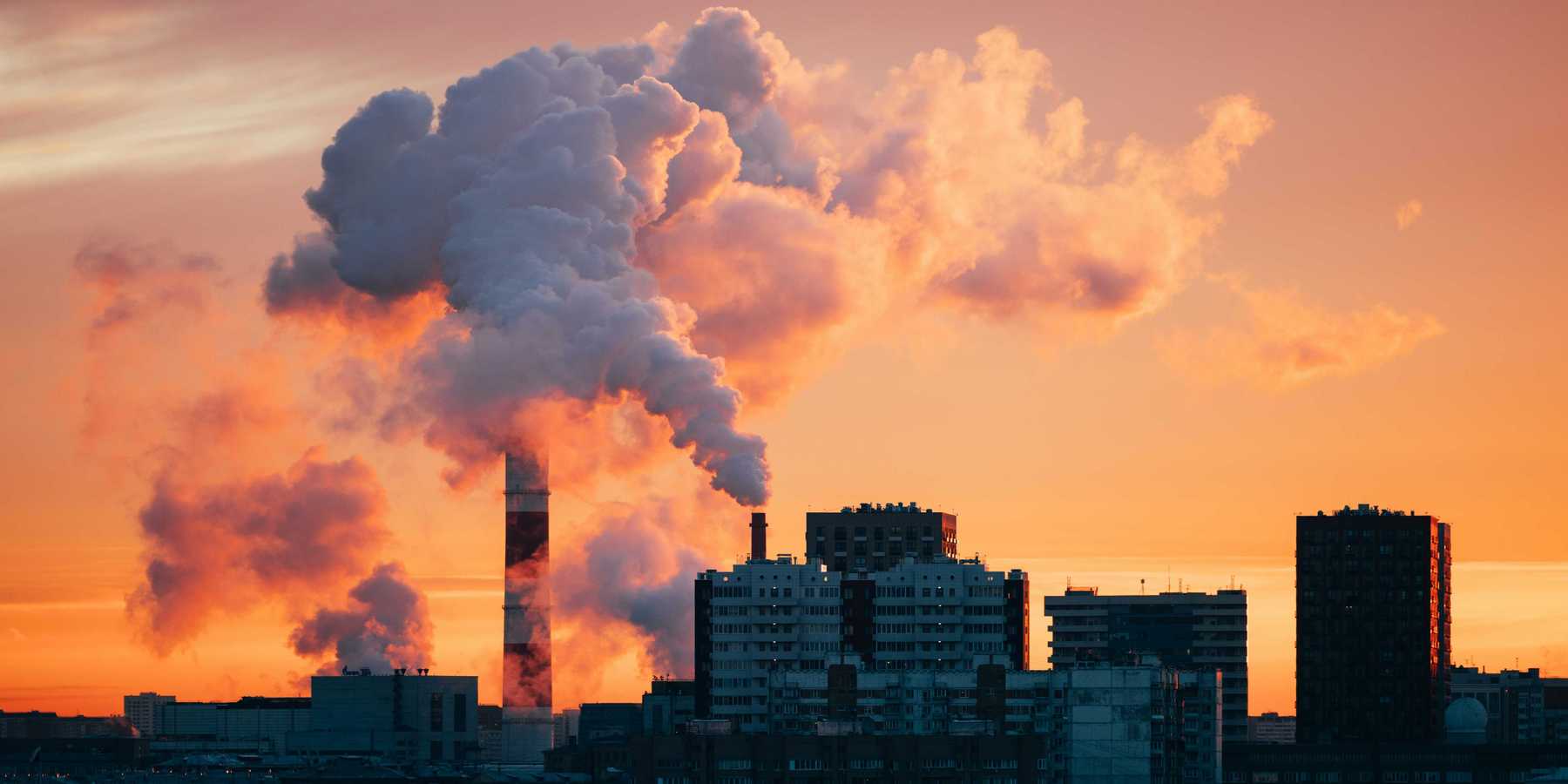 Factory smokestacks emitting smoke against sunset sky.