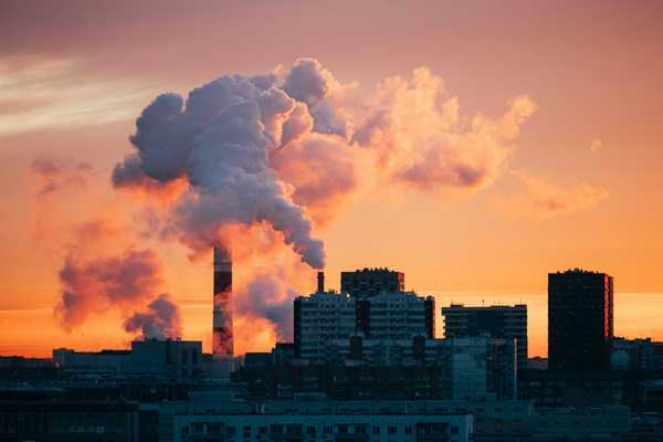 Factory smokestacks emitting smoke against sunset sky.