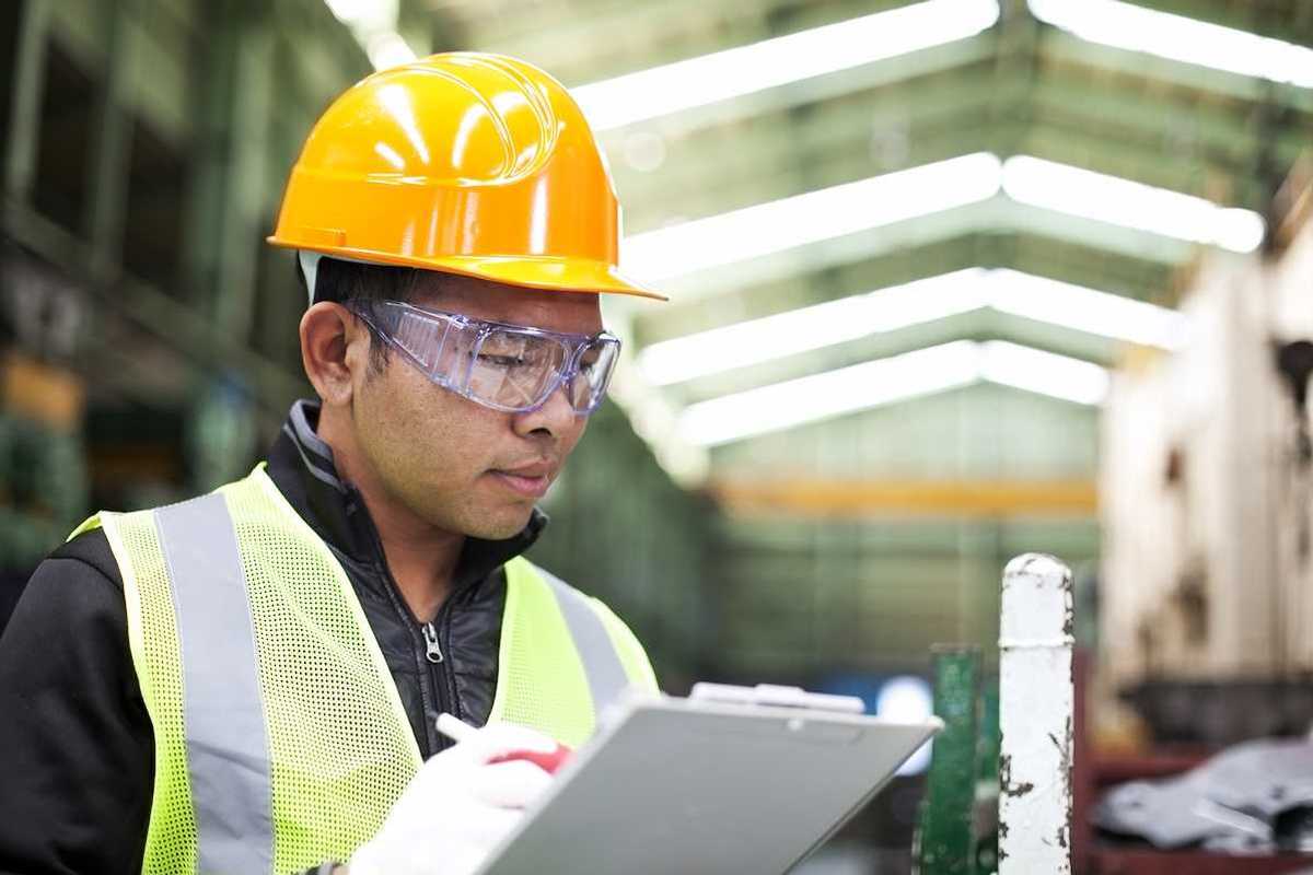 Factory worker writing on a clipboard while checking work