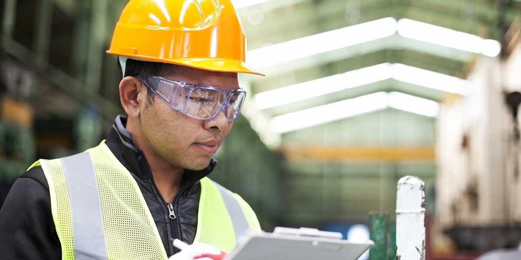 Factory worker writing on a clipboard while checking work
