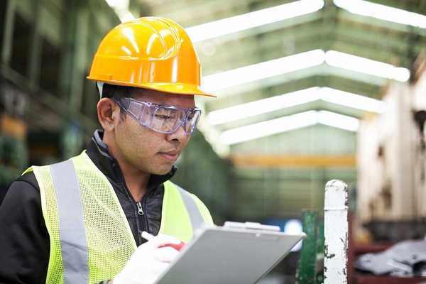 Factory worker writing on a clipboard while checking work