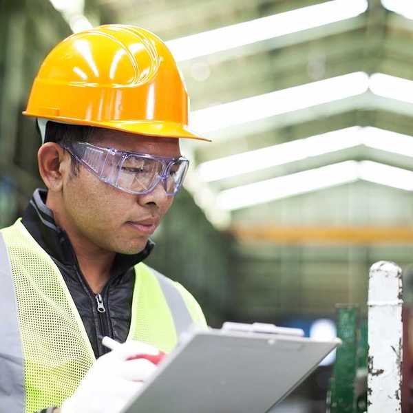 Factory worker writing on a clipboard while checking work