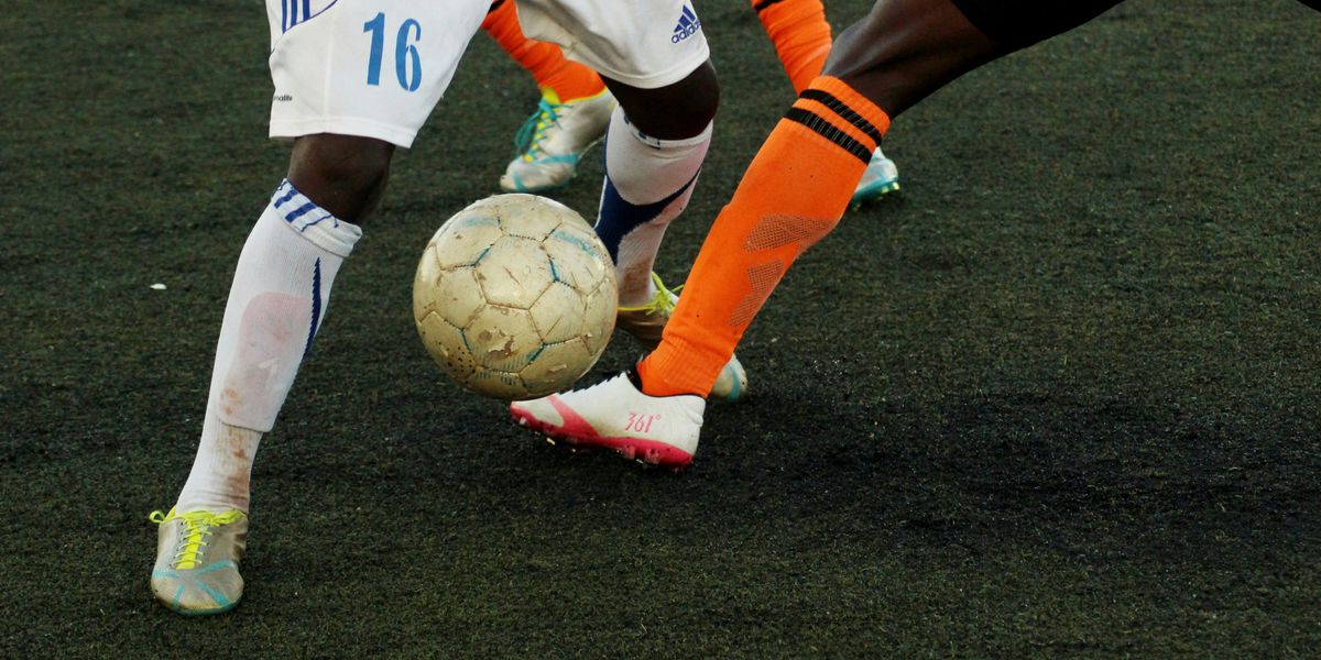 Feet of two people playing soccer with a ball in the middle.