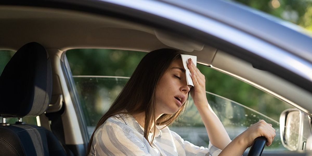 Female driver holding napkin or tissue to forehead on a hot day.