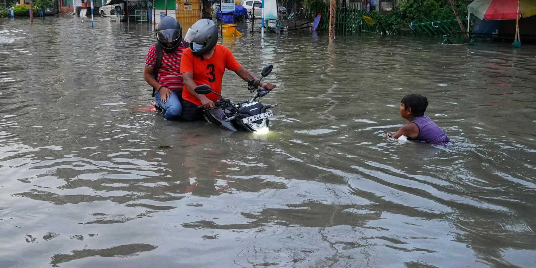 Filipinos navigating flooded street on motorcycle
