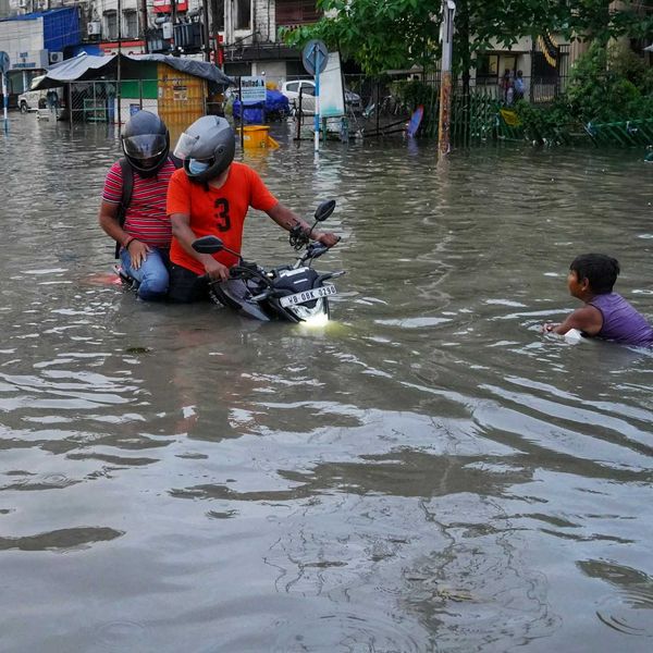 Filipinos navigating flooded street on motorcycle