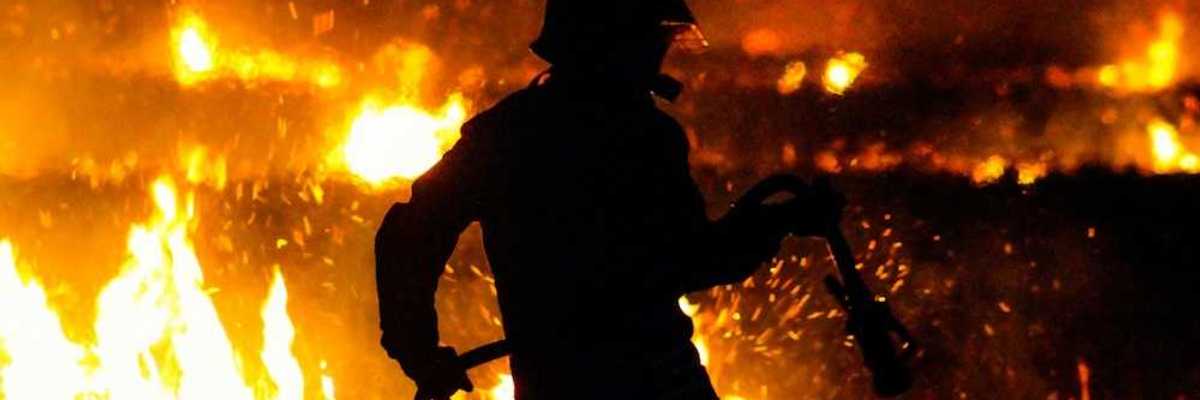 Firefighter silhouetted against flames at night