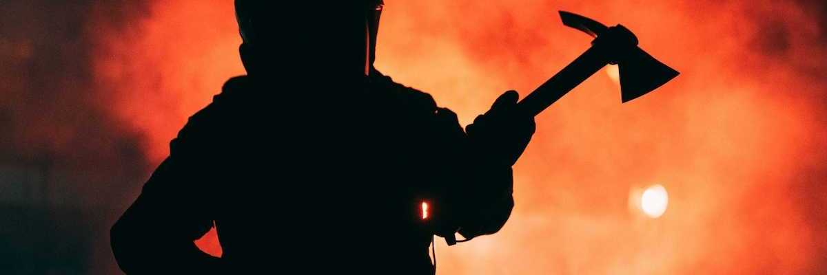 Firefighter wielding a Pulaski tool silhouetted against inferno