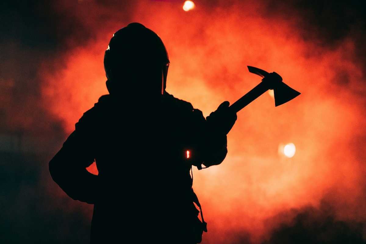 Firefighter wielding a Pulaski tool silhouetted against inferno