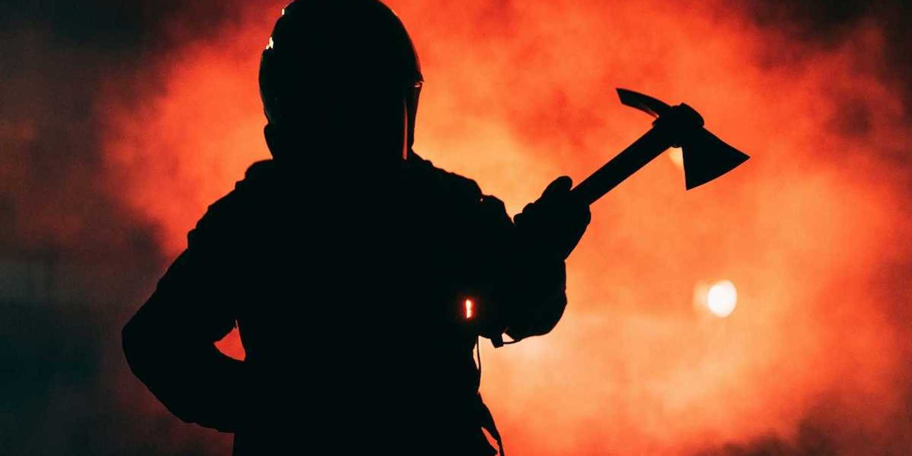 Firefighter wielding a Pulaski tool silhouetted against inferno