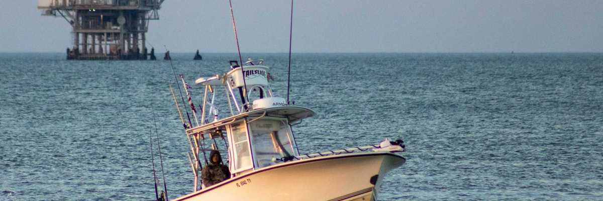 Fishing boat on open water with oil drilling rig in the background