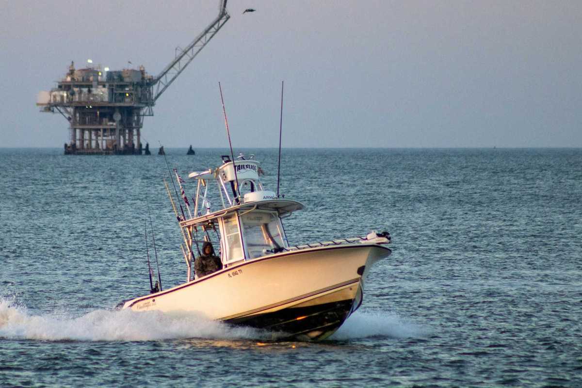 Fishing boat on open water with oil drilling rig in the background