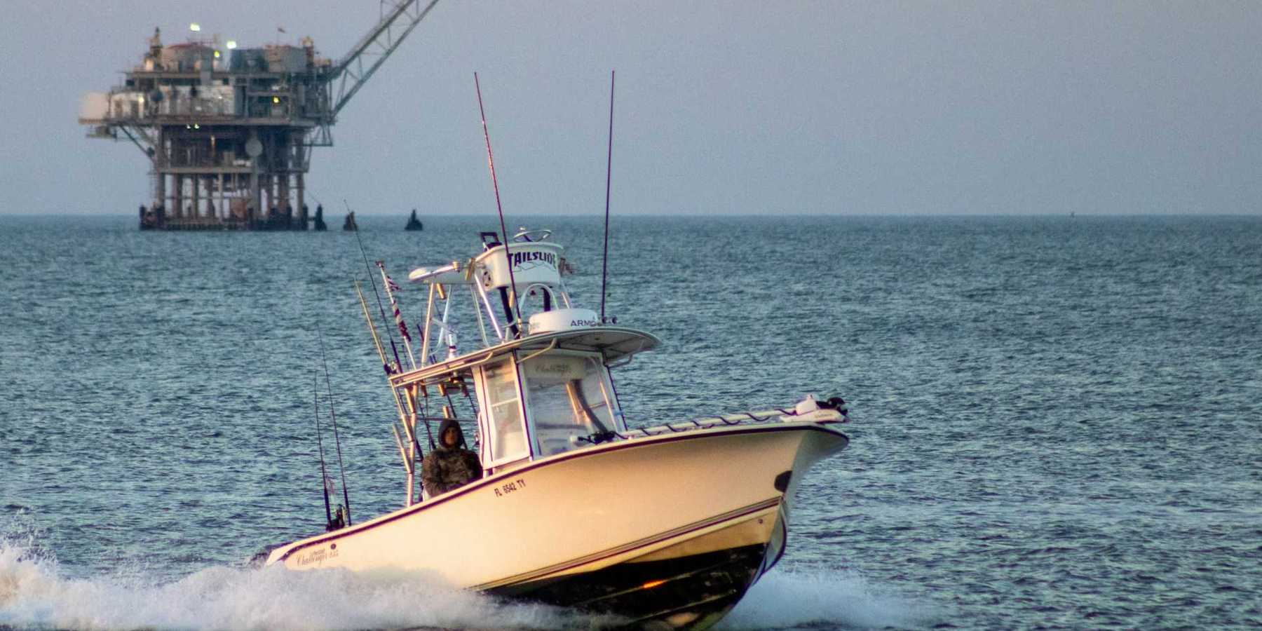 Fishing boat on open water with oil drilling rig in the background