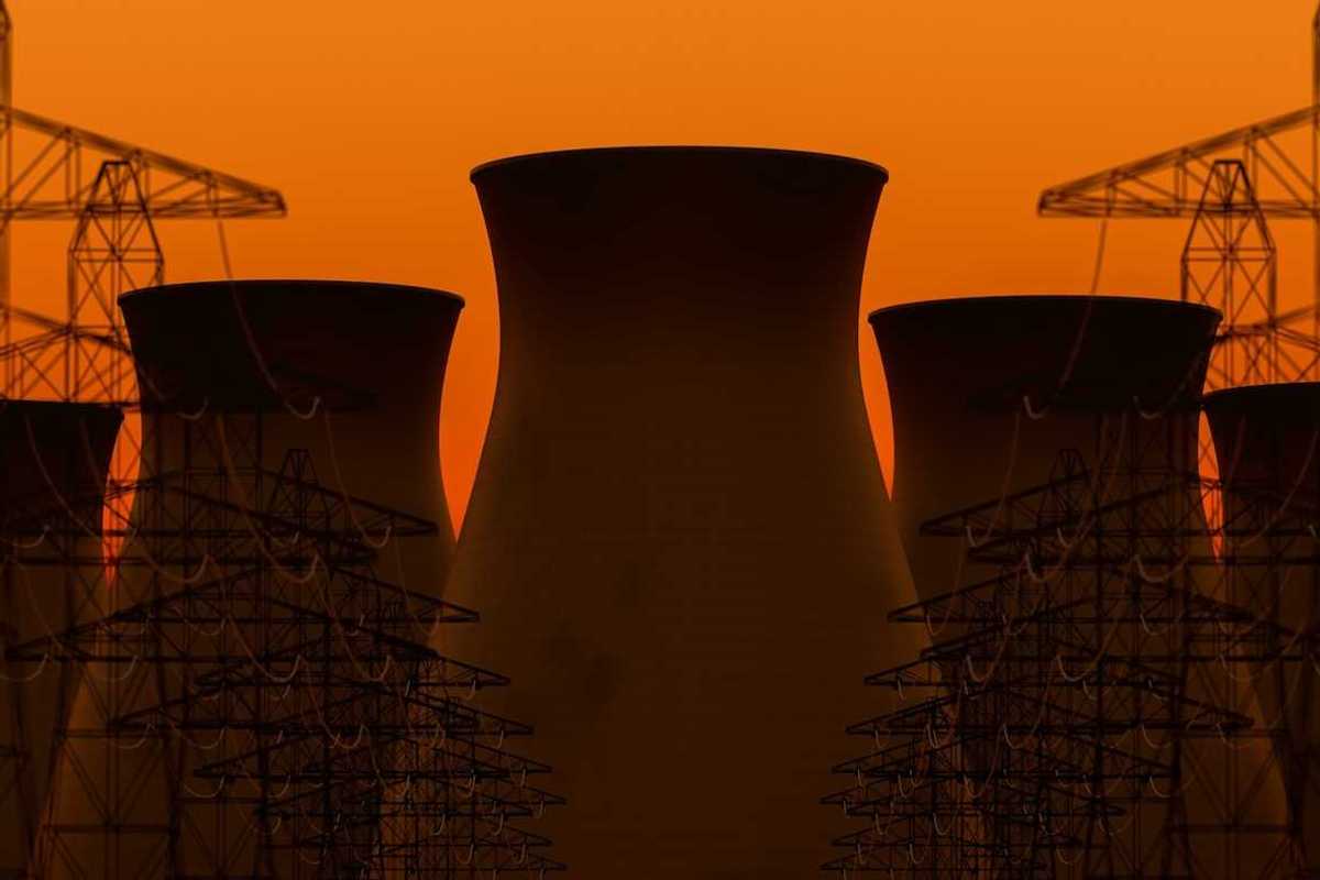 Five nuclear power plant cooling towers sillhouetted against transmission lines and orange sky
