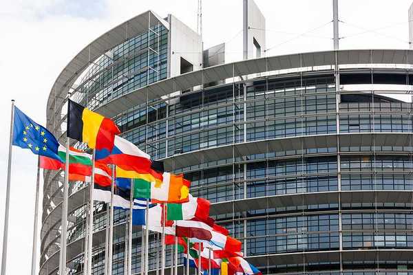 Flags of the EU flying outside a glass and steel building