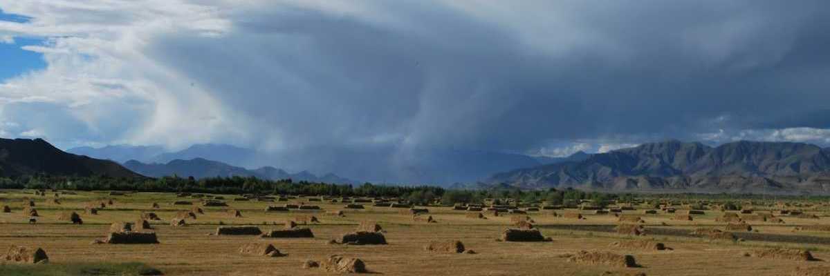 Flat valley in mountainous western state with haystacks and storm moving through valley