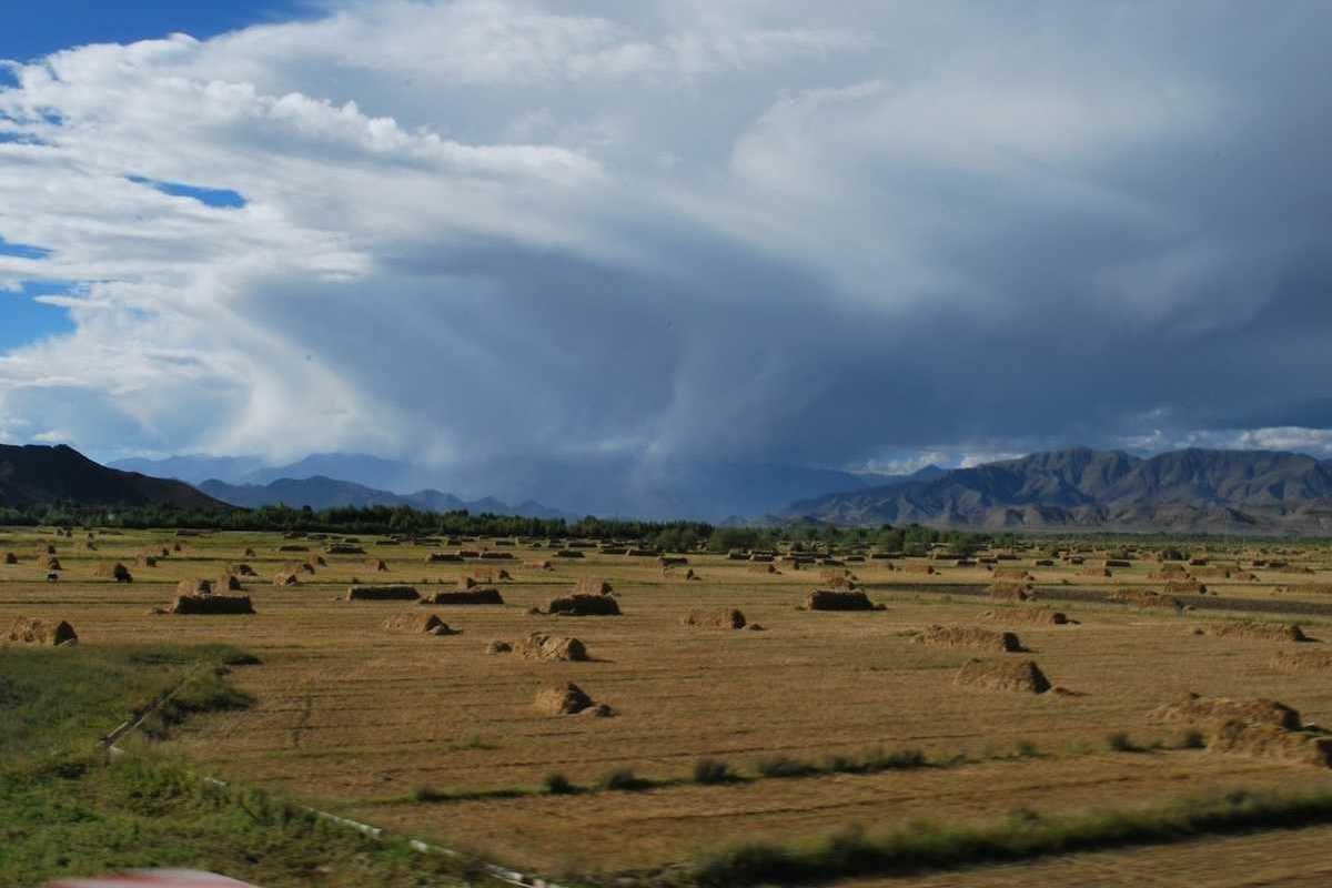 Flat valley in mountainous western state with haystacks and storm moving through valley