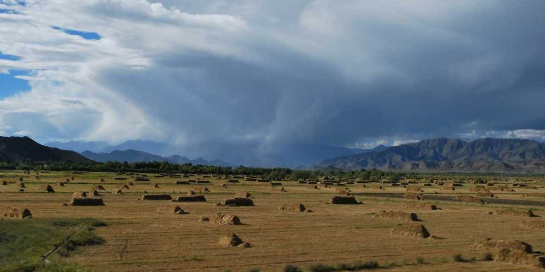 Flat valley in mountainous western state with haystacks and storm moving through valley