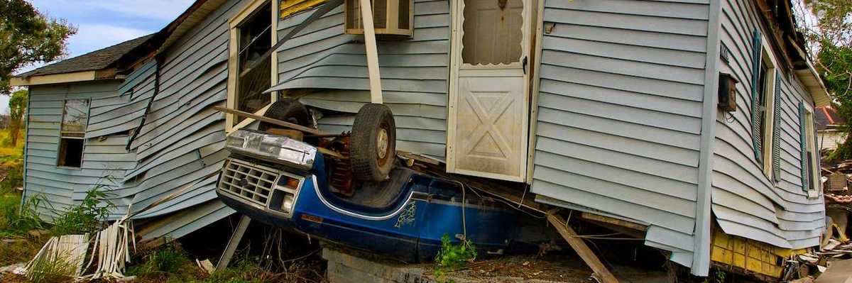 Flood aftermath with House sitting on an overturned blue Ford pickup truck.