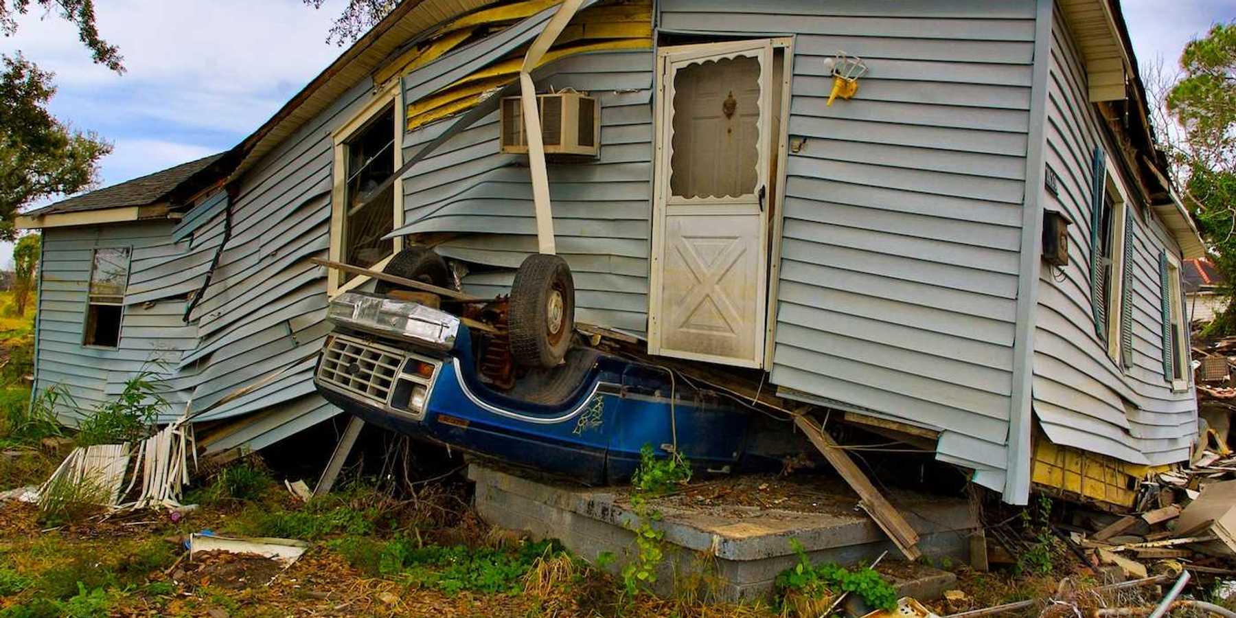 Flood aftermath with House sitting on an overturned blue Ford pickup truck.
