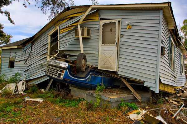 Flood aftermath with House sitting on an overturned blue Ford pickup truck.