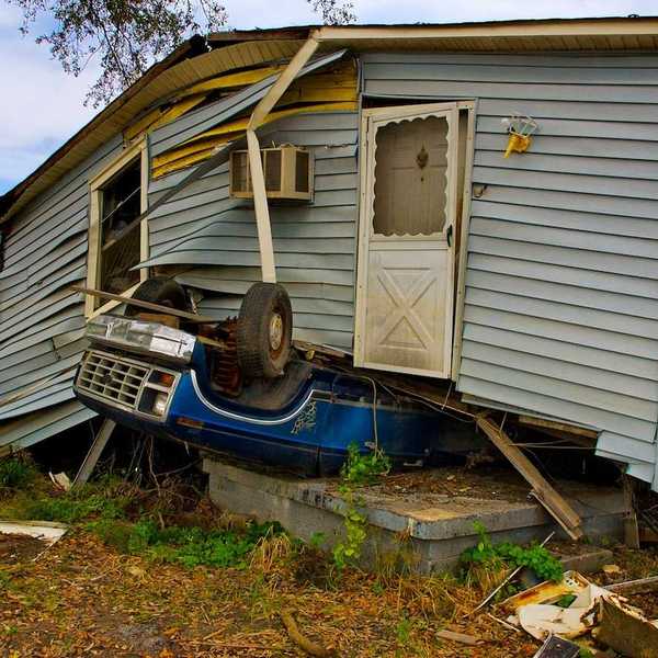 Flood aftermath with House sitting on an overturned blue Ford pickup truck.