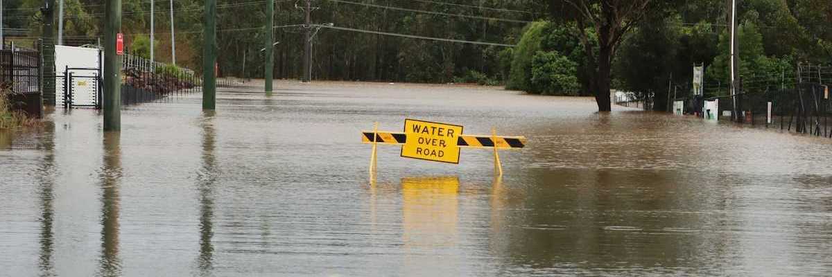 Flooded street with a yellow sign reading "water over road"
