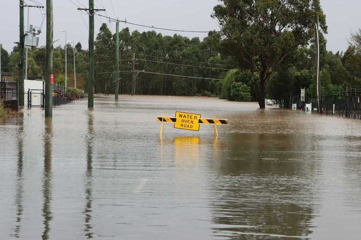 Flooded street with a yellow sign reading "water over road"