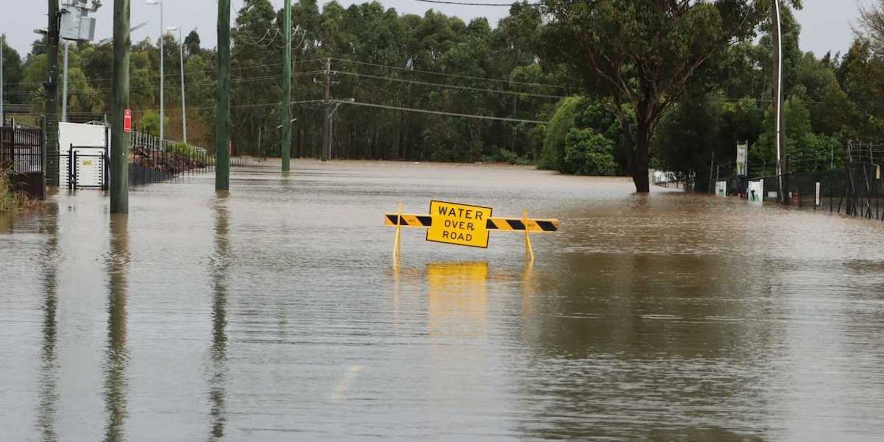 Flooded street with a yellow sign reading "water over road"