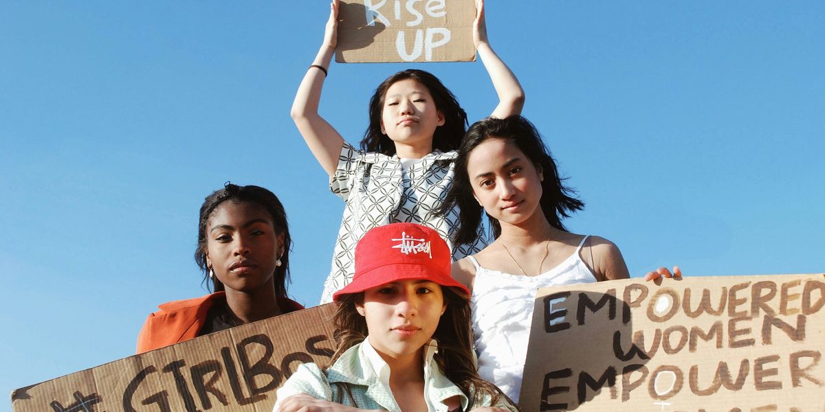 Four female protesters holding signs, one of which says We Rise Up
