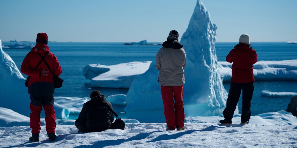 four people on ice near icebergs during daytime.
