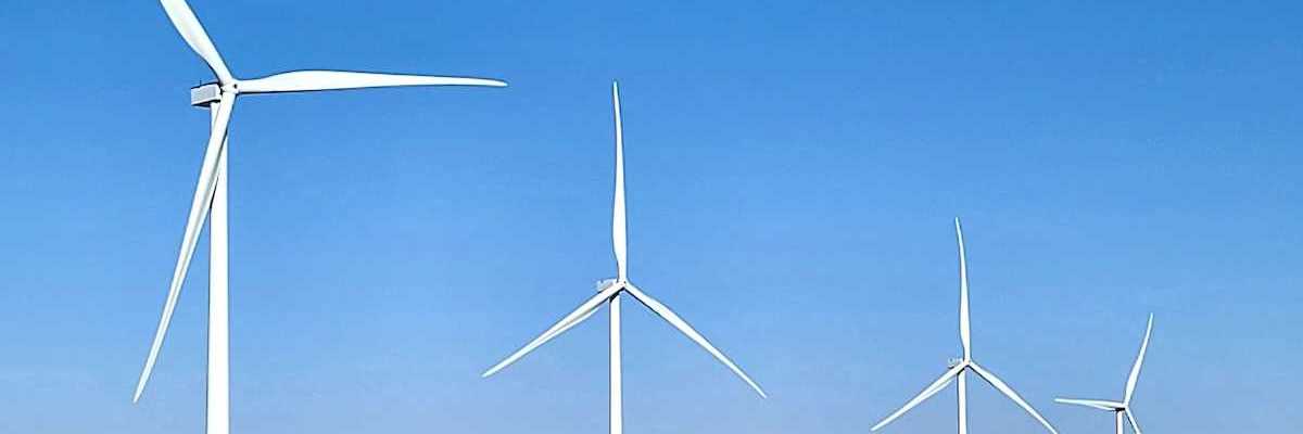 Four wind turbines in a row standing in a flat brown field.
