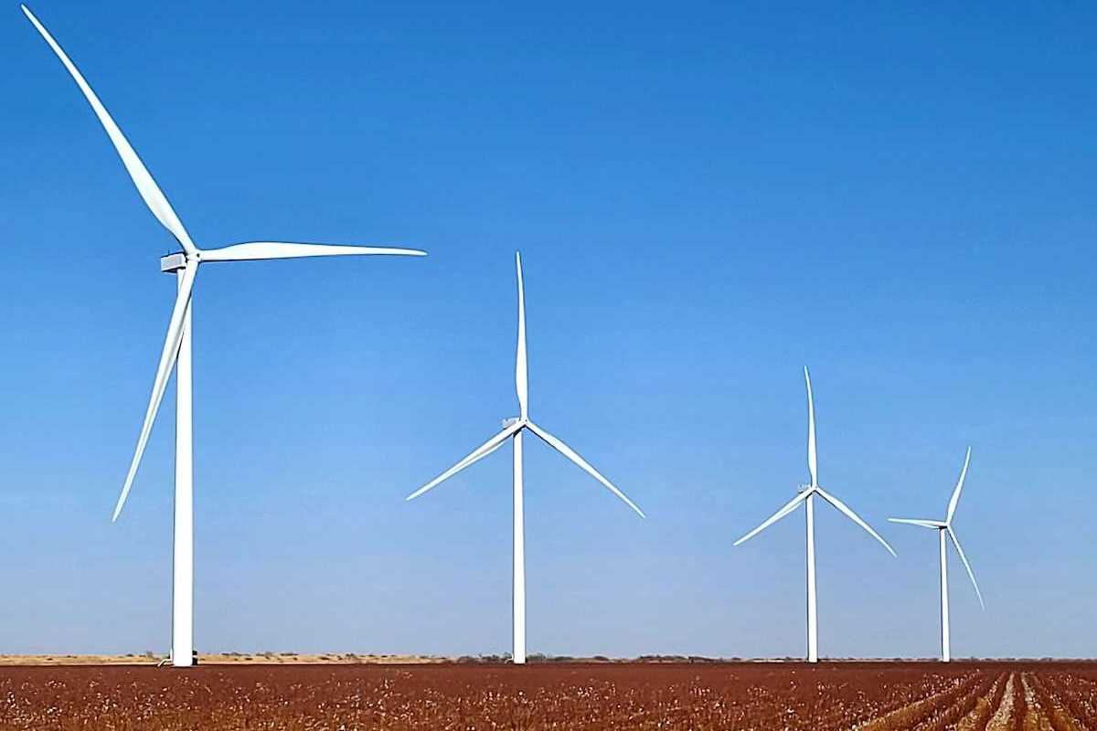 Four wind turbines in a row standing in a flat brown field.